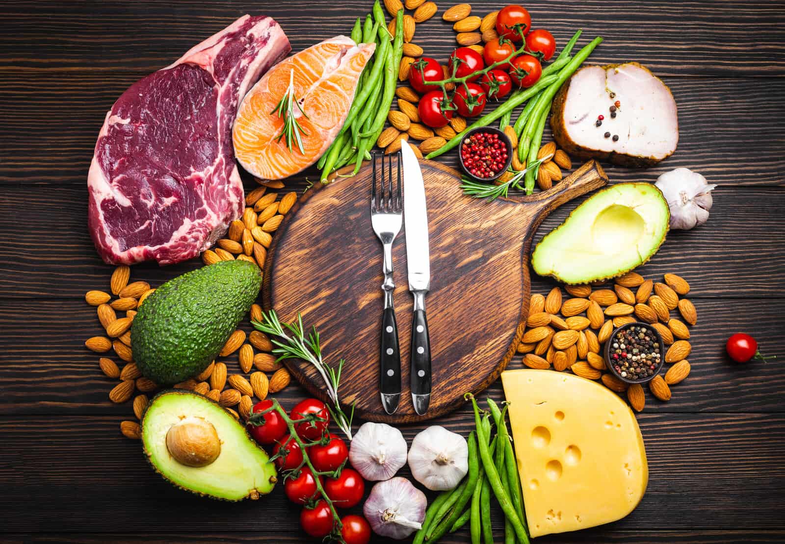 knife-and-fork-over-wooden-cutting-board-and-ketogenic-low-carbs-ingredients-for-healthy-eating-concept-and-weight-loss-top-view-keto-foods-meat-fish-avocado-cheese-vegetables-nuts
